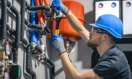 man-installs-heating-system-house-checks-pipes-with-wrench-min